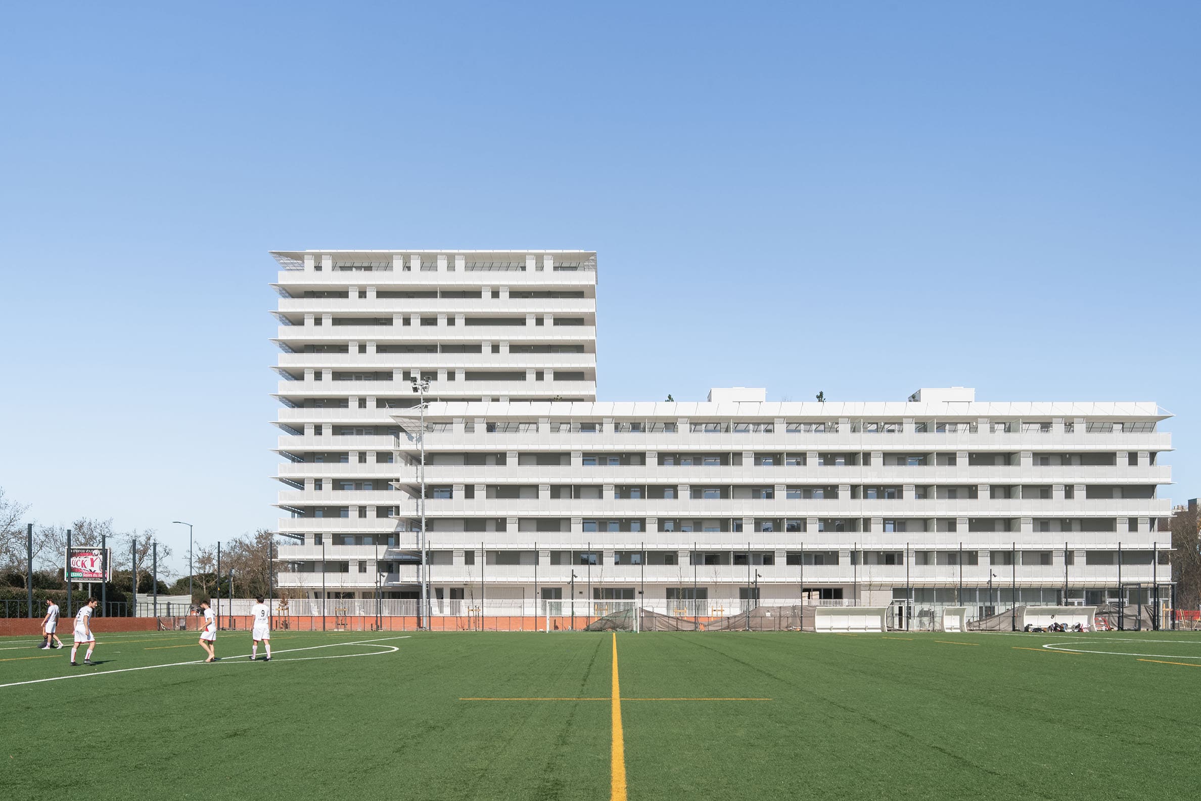 Blick auf zwei mehrstöckige, blockartige Wohngebäude, das hintere höher, davor ein Fußballplatz. CoBe, Belvedere und Präriegebäude, Toulouse, Foto: Cédric Colin