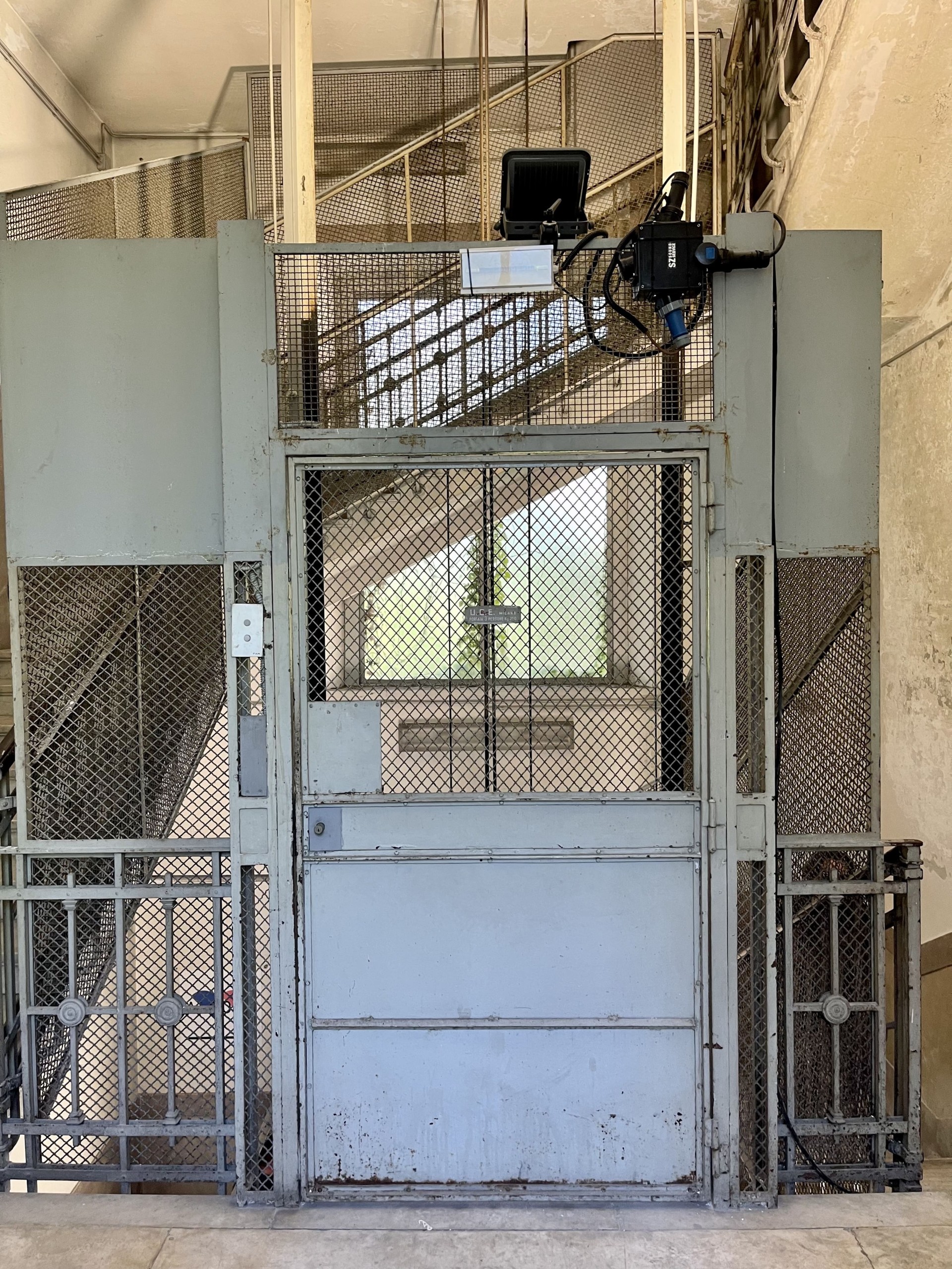 Blick auf ein Treppenhaus mit einem Metallgitter und einer Metalltür. Alcova 2022, Foto: Baumeister/Fabian Peters