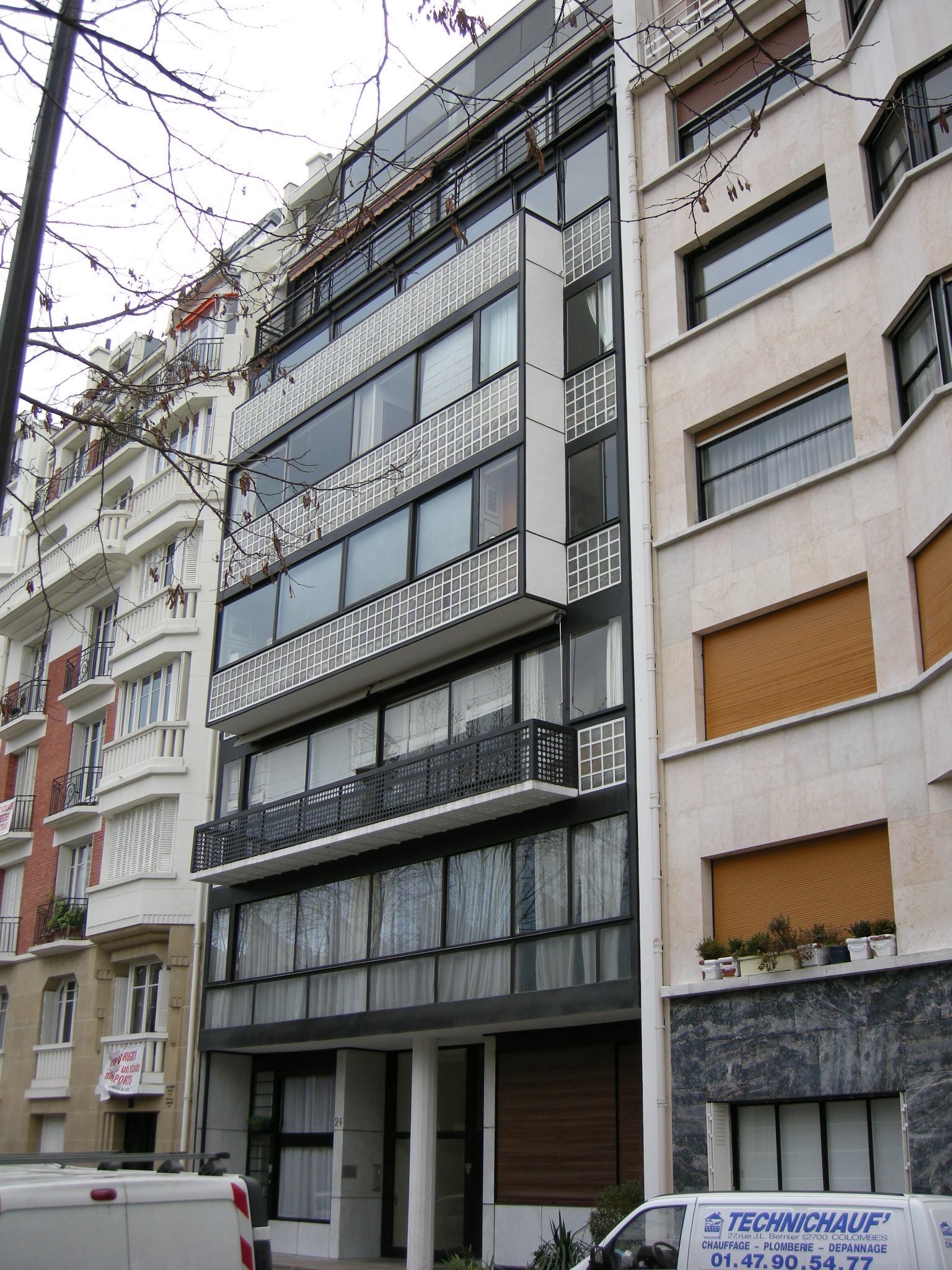 Blick auf eine Häuserzeile mit drei Häusern, wovon das mittlere viele Glasbausteine enthält.