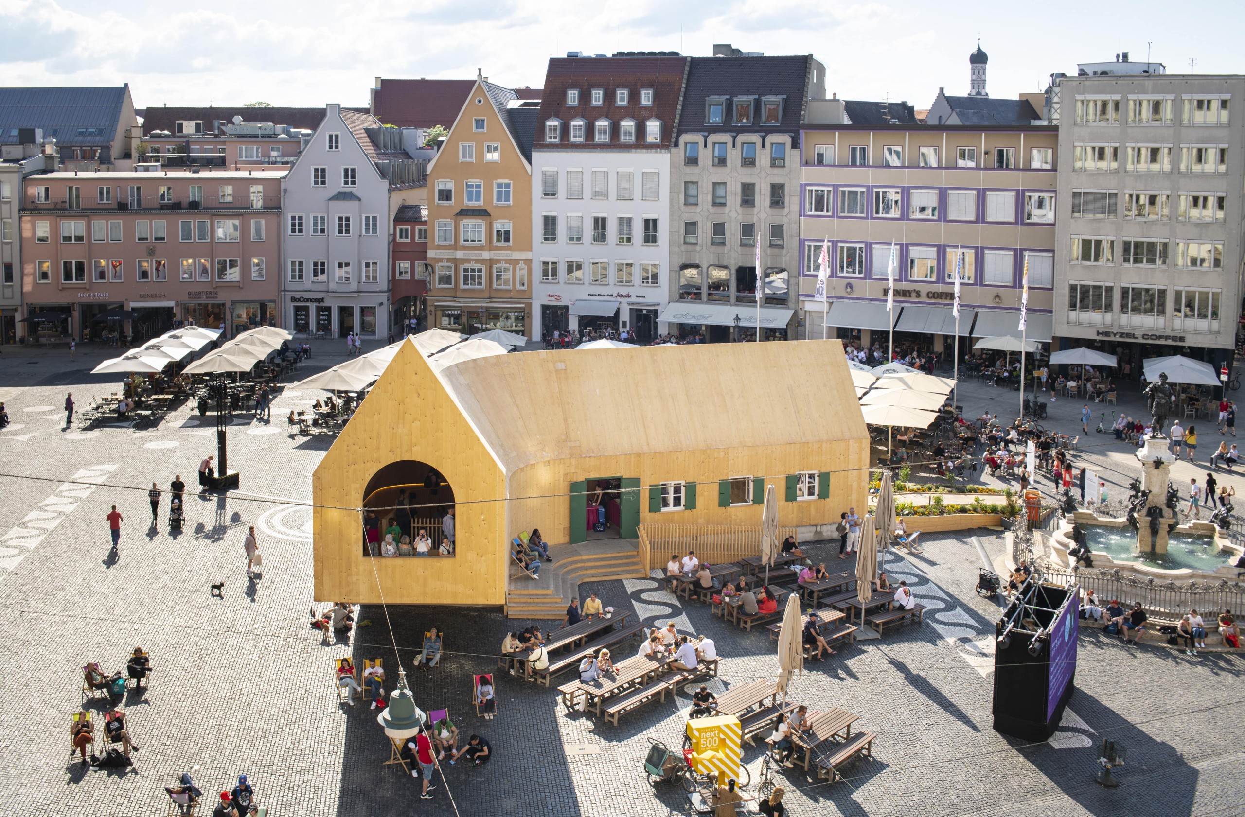 Blick auf einen hölzernen Pavillon auf einem Platz in der Stadt Augsburg anlässlich des Fests „500 Jahre Fuggerei“. MVRDV, NEXT500 Pavillon, Augsburg, Foto: © Saskia Wehler