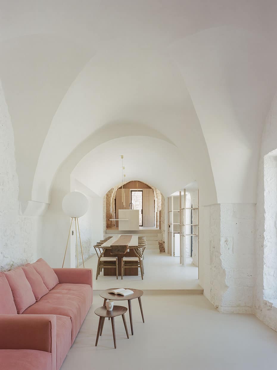 Blick in einen länglichen, weiß gestrichenen Raum mit Gewölbe, darin links ein rotes Sofa, dahinter ein langer Tisch mit mehreren Stühlen. Valari, Masseria Belvedere, Carovigno, Foto: ©Lorenzo Zandri