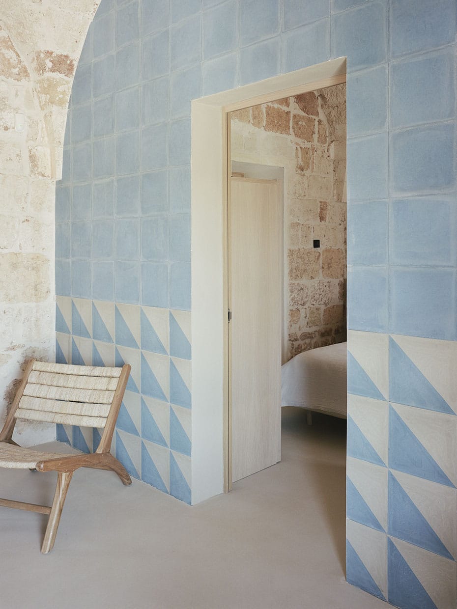 Blick auf eine Wand mit hellblauen und weißen Fließen, darin eine Türöffnung, davor ein Stuhl. Valari, Masseria Belvedere, Carovigno, Foto: ©Lorenzo Zandri