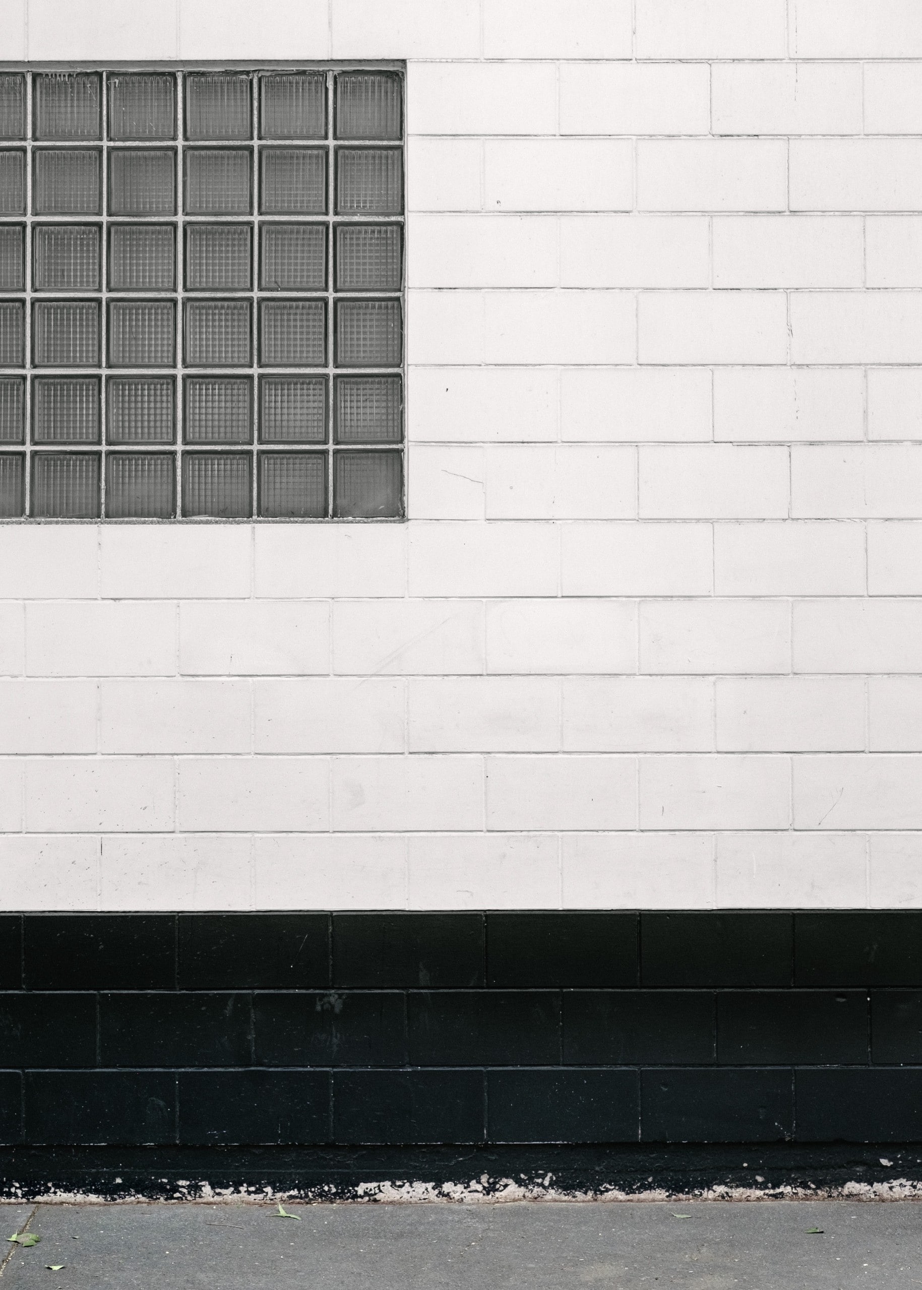 Weiß-schwarze Mauer mit einem angeschnittenen Fenster aus Glasbausteinen. Foto: Alex Rodríguez Santibáñez on Unsplash