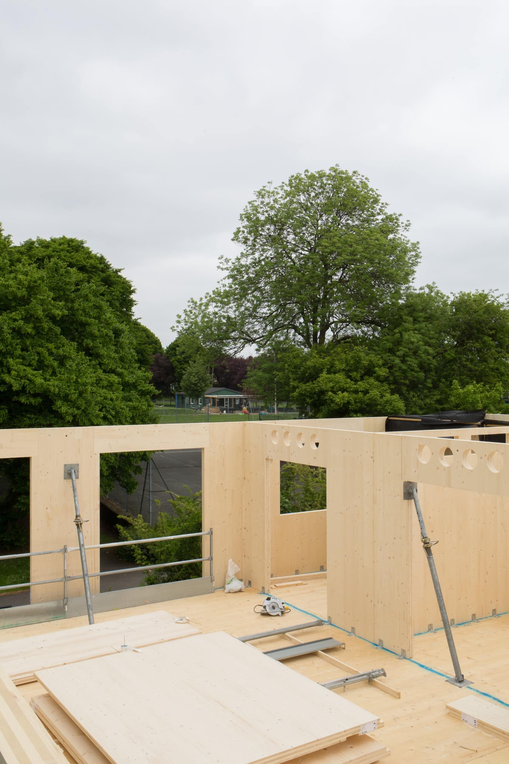 Blick von oben auf die Baustelle eines Holzhauses, im Hintergrund Bäume. Dyvik Kahlen Architects, Kindergarten und Gemeindezentrum, London, Foto: Antoine Espinasseau
