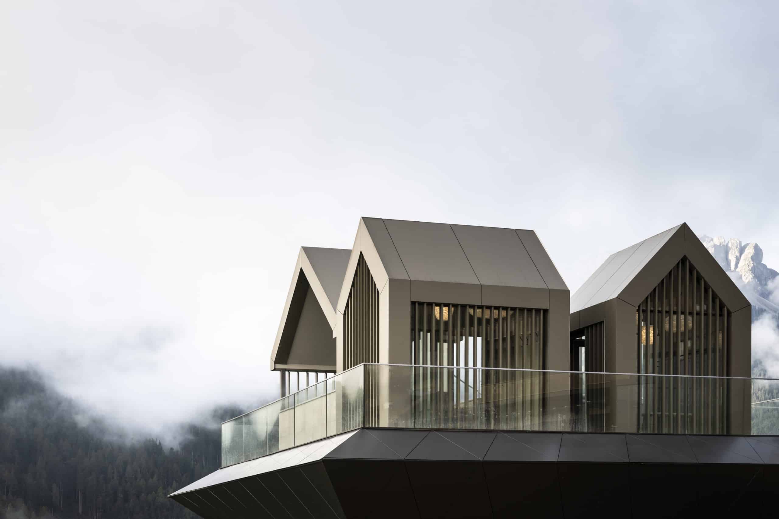 Blick auf drei kleine Hütten mit Satteldach auf einer Plattform, im Hintergrund Wolken und eine Bergspitze. Noa* Network of Architecture, Hub of Huts, Hotel Hubertus Olang, Foto: ©AlexFilz