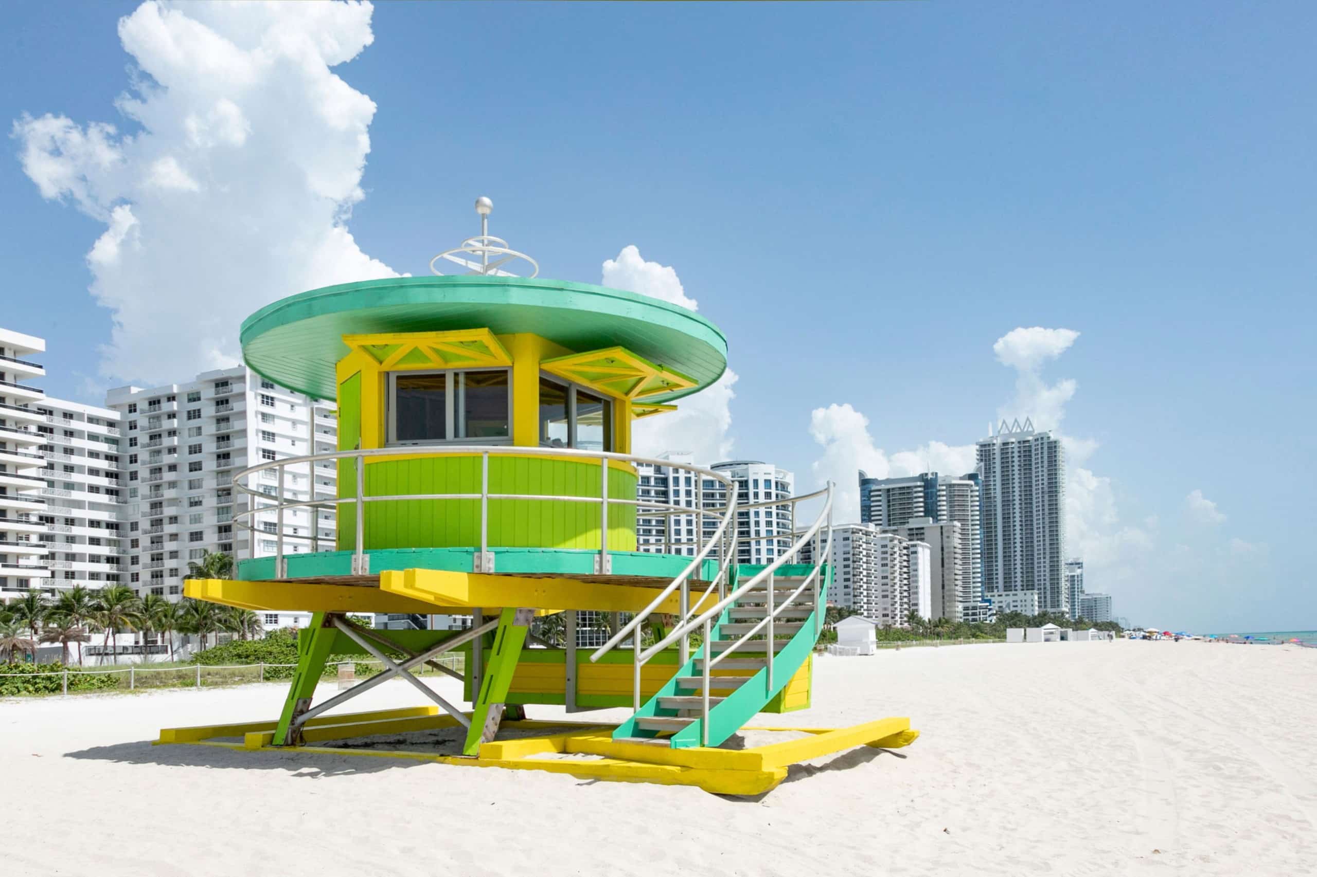 Ein rundes Strandwächterhäuschen in Grüntönen und Gelb am Strand, im Hintergrund mehrere Hochhäuser. Miami Beach, Lifeguard Tower, William Lane, Foto: Archiv Architekten